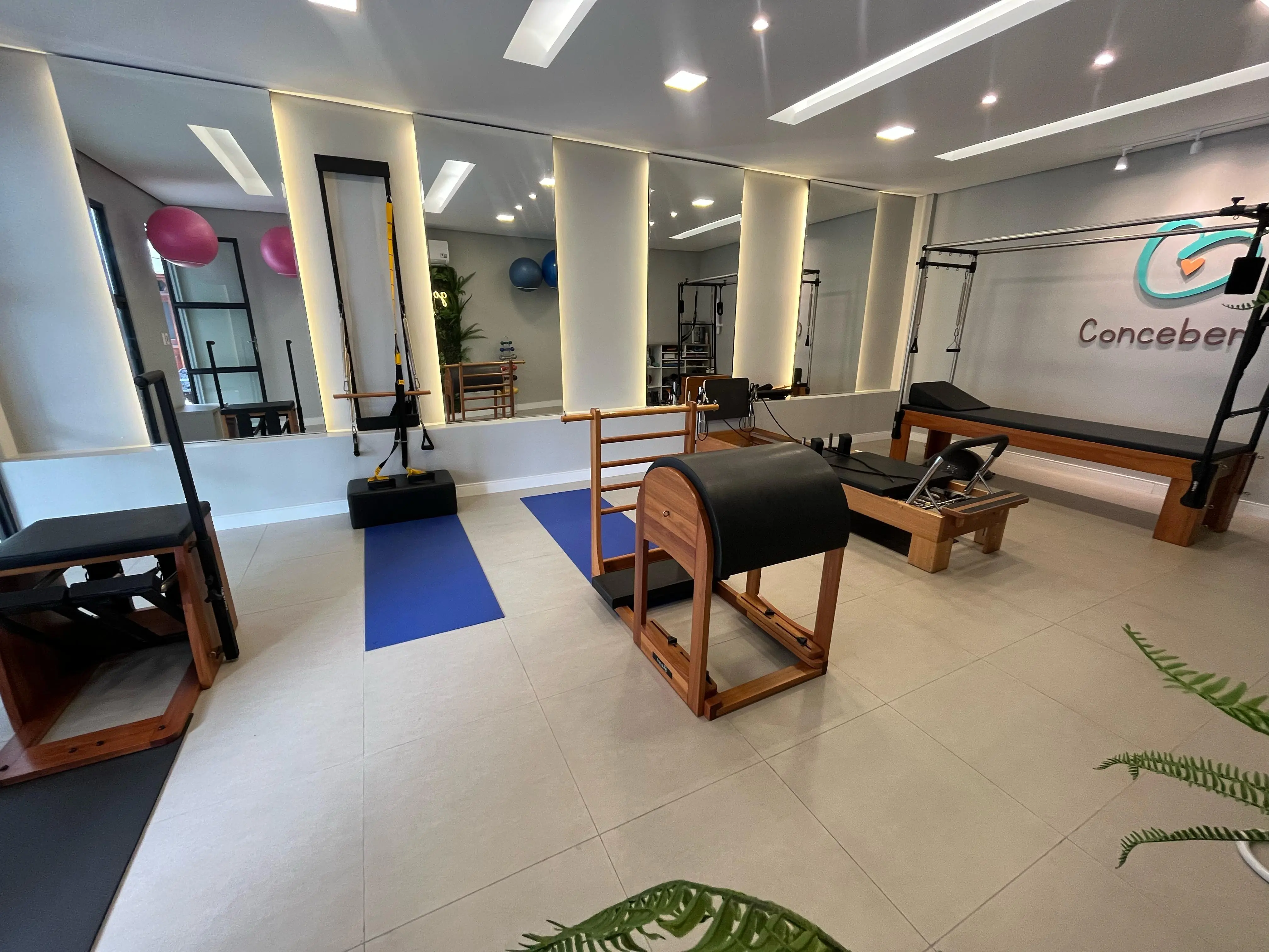 Sala de Pilates com tapetes, barras e aparelhos, iluminada e organizada
